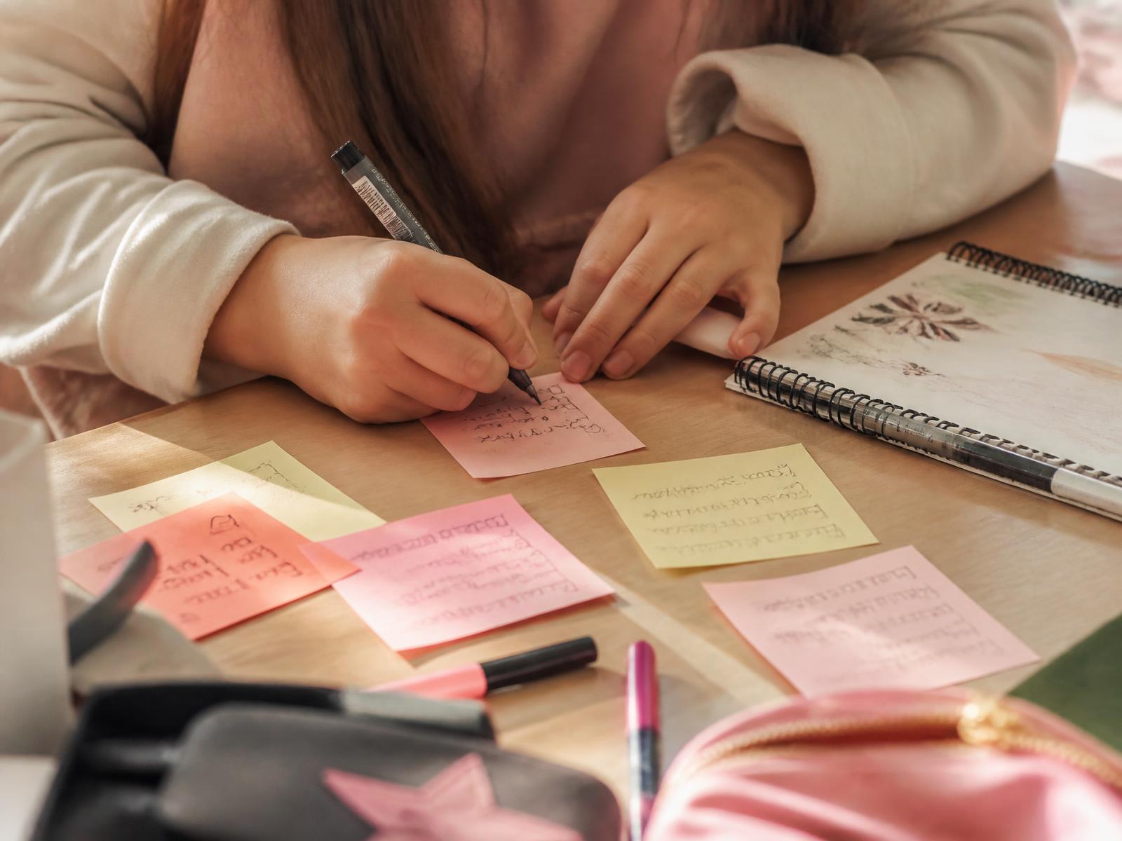 Handen van een meid die haar eerste idee op een post-it schrijft